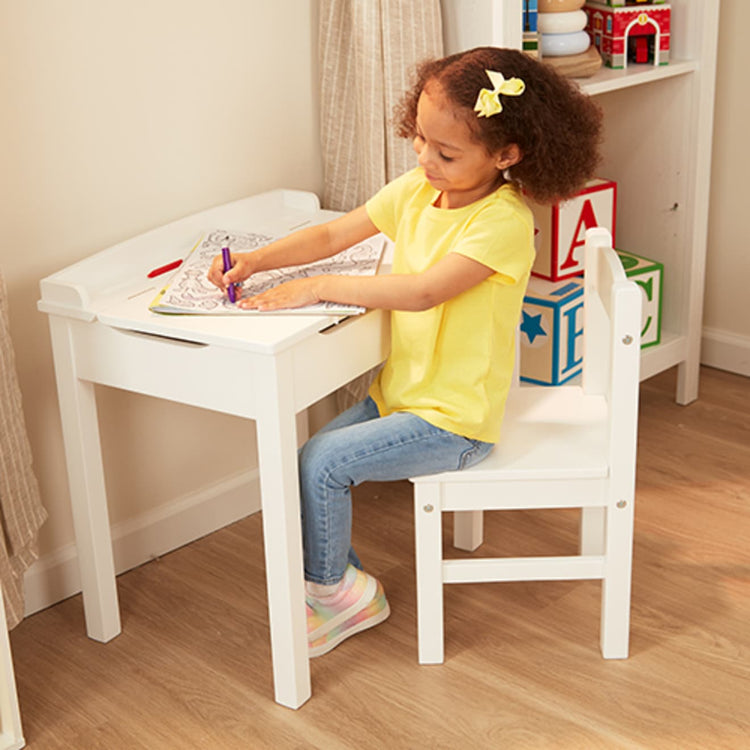 A kid playing with the Melissa & Doug Wooden Child's Lift-Top Desk & Chair - White