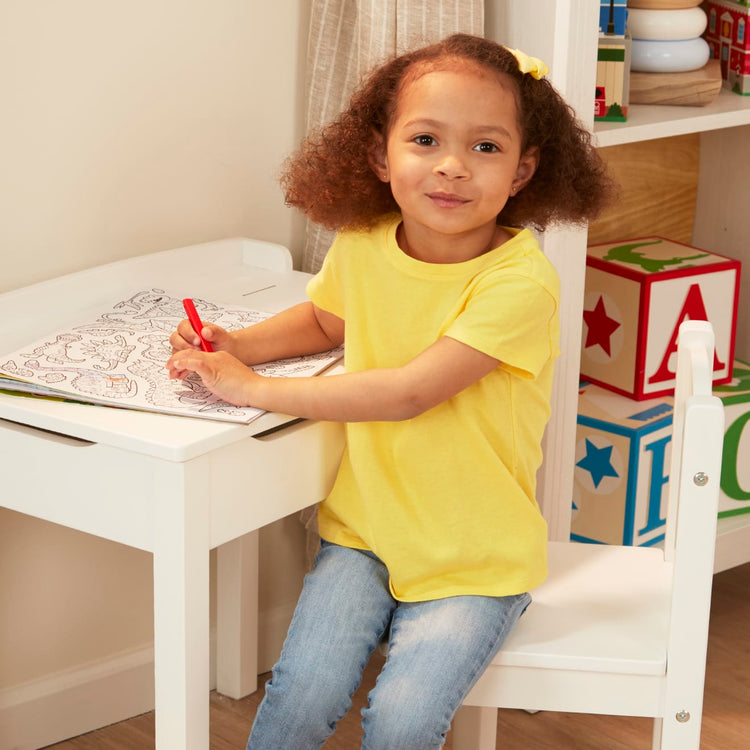 A kid playing with the Melissa & Doug Wooden Child's Lift-Top Desk & Chair - White