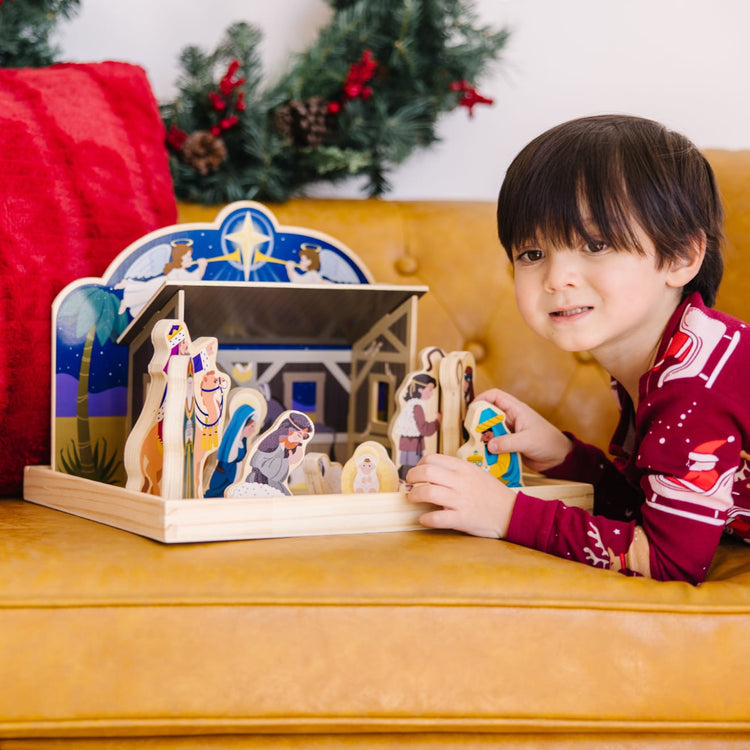 A kid playing with the Melissa & Doug Classic Wooden Christmas Nativity Set With 4-Piece Stable and 11 Wooden Figures
