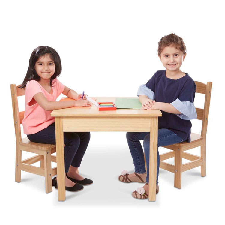 A child on white background with the Melissa & Doug Solid Wood Table and 2 Chairs Set - Light Finish Furniture for Playroom
