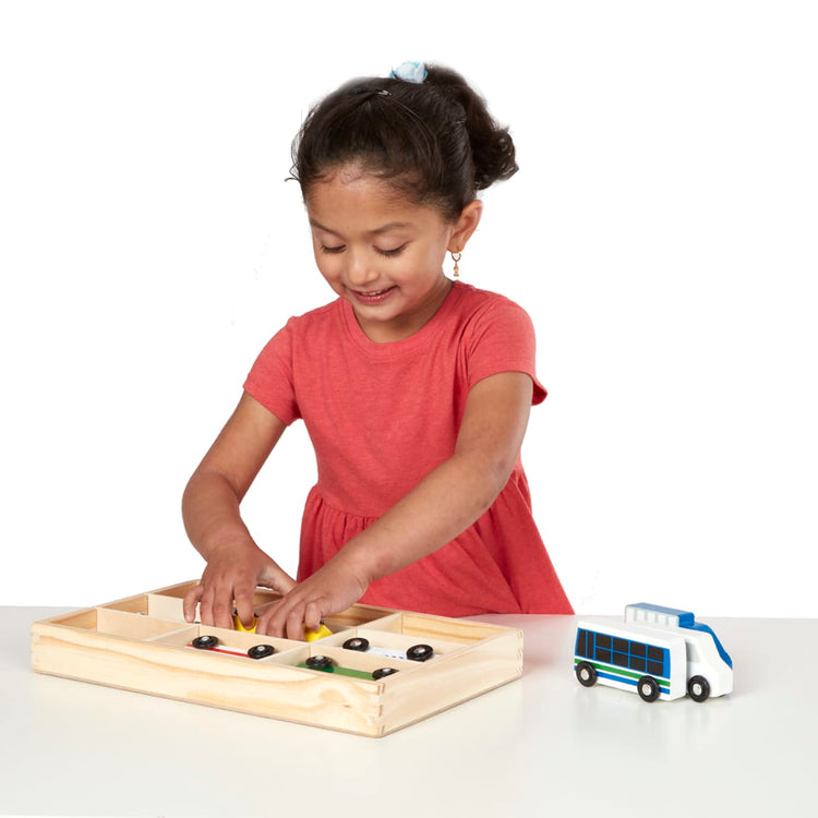 A child on white background with the Melissa & Doug Wooden Town Vehicles Set in Wooden Tray (9 pcs)