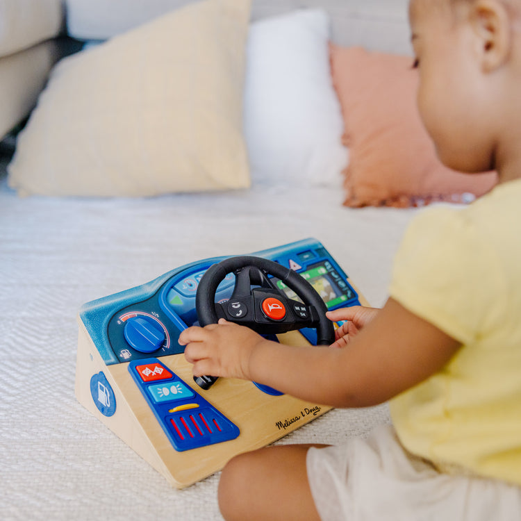 A kid playing with The Melissa & Doug Vroom & Zoom Interactive Wooden Dashboard Steering Wheel Pretend Play Driving Toy