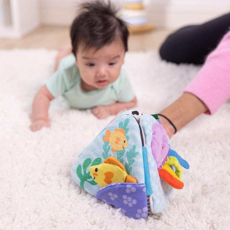 A kid playing with The Melissa & Doug Ocean Tummy Time Triangle Infant Baby Toy, Soft Sensory Toy with Textures, Mirror, Floor Toy for Newborns to Ages 6 Months