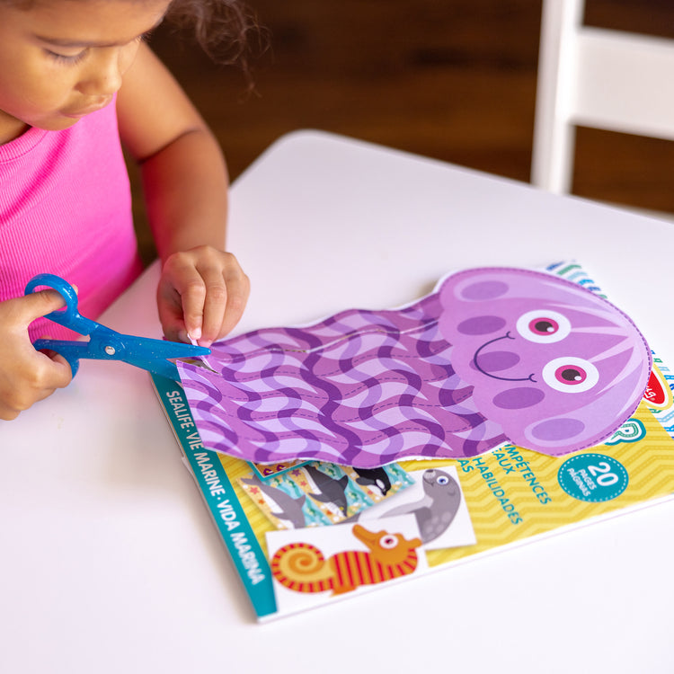 A kid playing with The Melissa & Doug Sea Life Scissor Skills Activity Pad with Child-Safe Scissors – 20 Pages