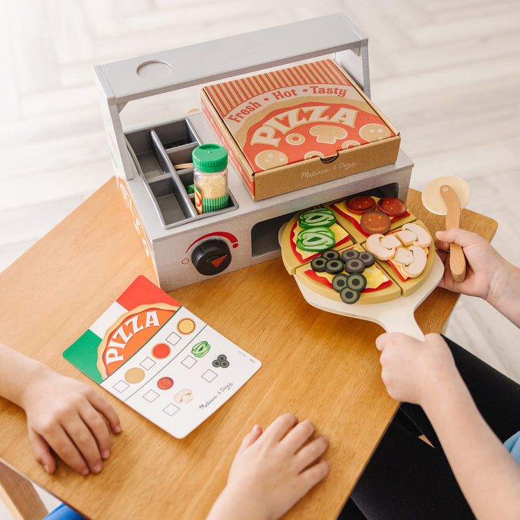 A kid playing with The Melissa & Doug Top & Bake Wooden Pizza Counter Play Set (41 Pcs)