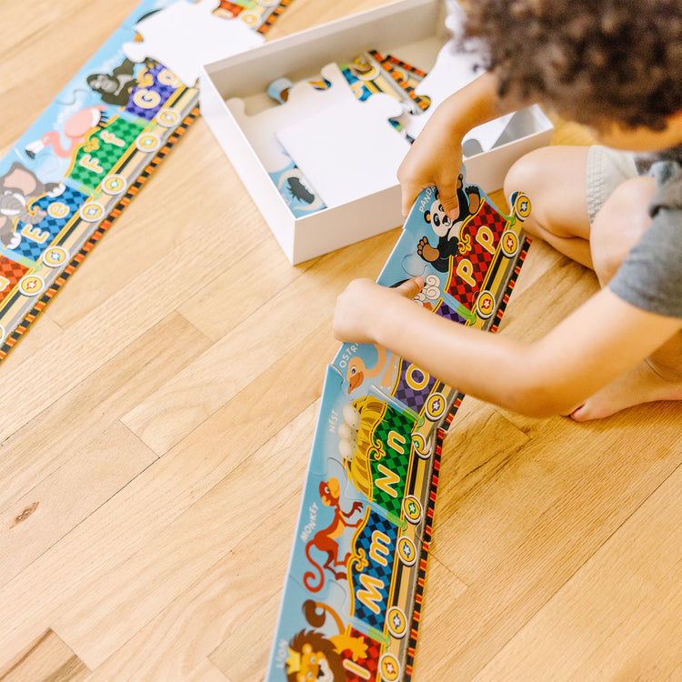 A kid playing with The Melissa & Doug Alphabet Express Jumbo Jigsaw Floor Puzzle (27 pcs, 10 feet long)