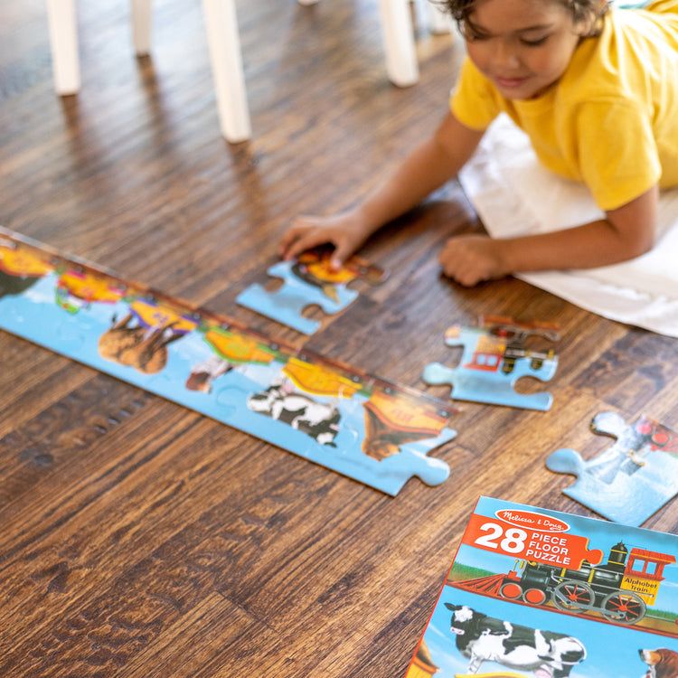 A kid playing with The Melissa & Doug Alphabet Train Jumbo Jigsaw Floor Puzzle - Letters and Animals (28 pcs, 10 feet long)