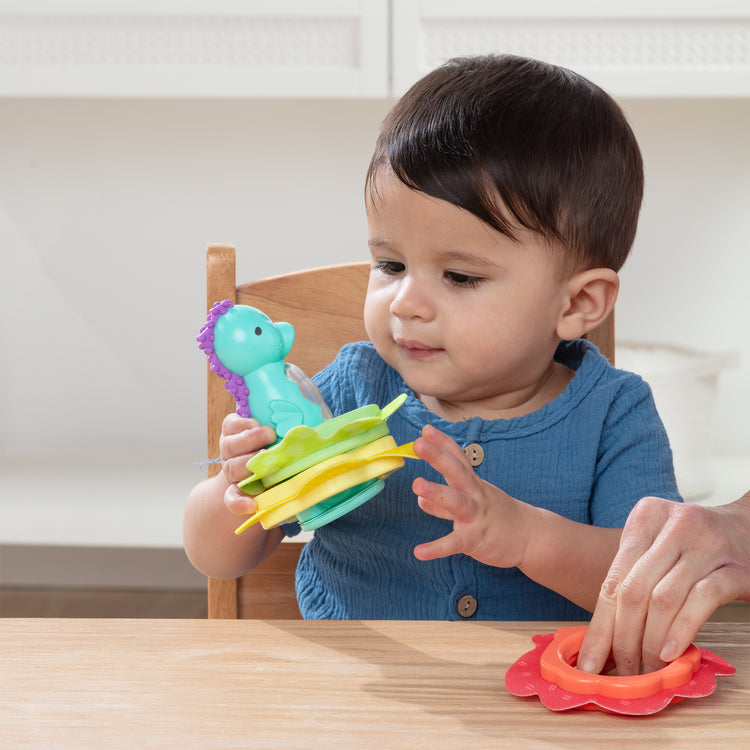 A kid playing with The Melissa & Doug Ocean Waves Press & Stack Seahorse Stacking Toy with 3 Sensory Rings - Rattle for Babies 10 Months+