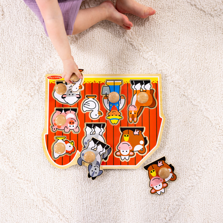 A kid playing with The Melissa & Doug Farm Animals Jumbo Knob Wooden Puzzle