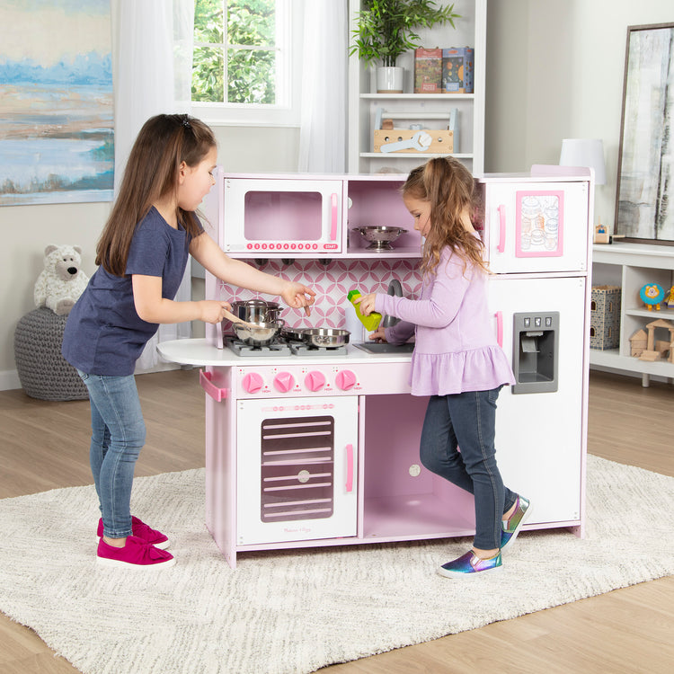 A kid playing with The Melissa & Doug Wooden Chef’s Pretend Play Toy Kitchen With “Ice” Cube Dispenser – Cupcake Pink/White