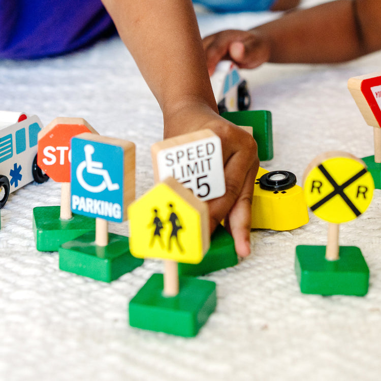 A kid playing with The Melissa & Doug Wooden Vehicles and Traffic Signs With 6 Cars and 9 Signs