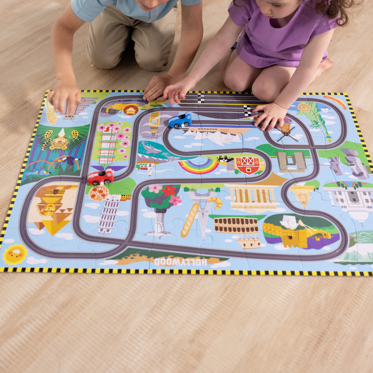 A kid playing with The Melissa & Doug Race Around the World Tracks Cardboard Jigsaw Floor Puzzle and Wind-Up Vehicles – 48 Pieces, for Boys and Girls 3+