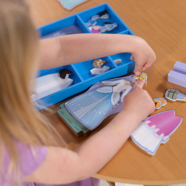 A kid playing with The Melissa & Doug Disney Princess Cinderella Magnetic Dress-Up Wooden Doll Pretend Play Set (30+ pcs)