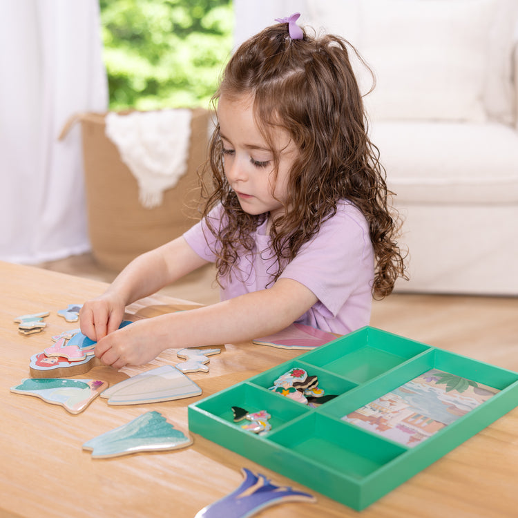 A kid playing with The Melissa & Doug Disney Princess Ariel Magnetic Dress-Up Wooden Doll Pretend Play Set (30+ Pieces)