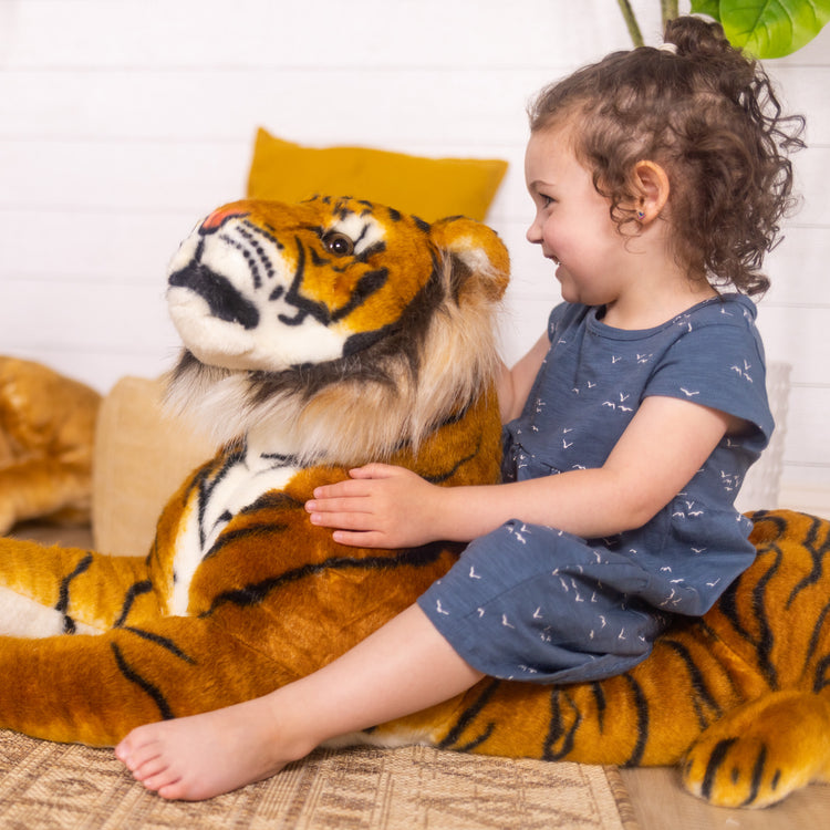 A kid playing with The Melissa & Doug Giant Tiger - Lifelike Stuffed Animal, Over 5 Feet Long (Includes Tail)