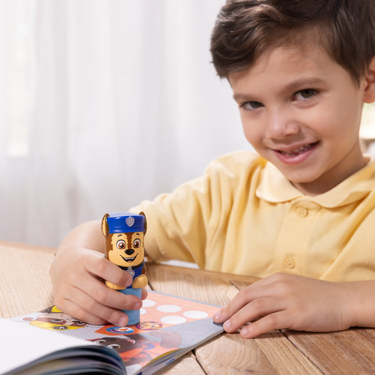 A kid playing with The Melissa & Doug Sticker WOW!™ PAW Patrol Chase Bundle: 24-Page Activity Pad, Sticker Stamper, 500 Stickers, Mini Pad, Arts and Crafts Fidget Toy Collectible Character