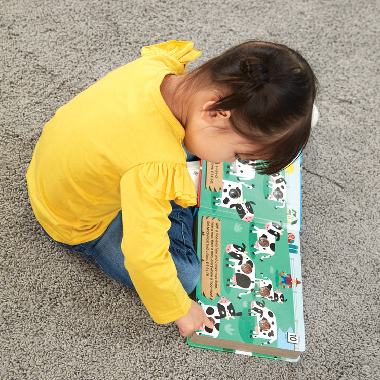 A kid playing with The Melissa & Doug Children's Book - Poke-a-Dot: Old MacDonald’s Farm (Board Book with Buttons to Pop)