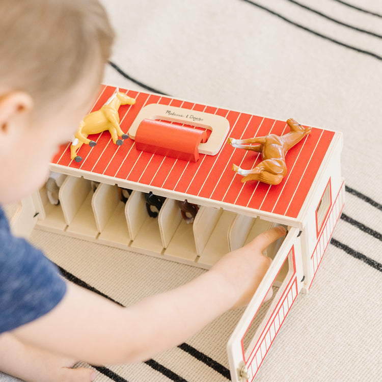 A kid playing with The Melissa & Doug Take-Along Show-Horse Stable Play Set With Wooden Stable Box and 8 Toy Horses