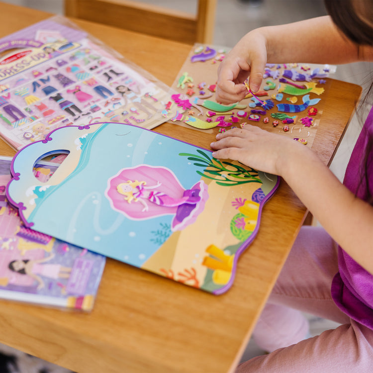 A kid playing with The Melissa & Doug Puffy Sticker Activity Books Set: Dress-Up, Princess, Mermaid - 208 Reusable Stickers