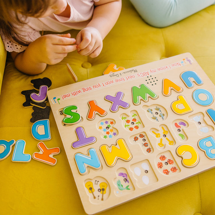 A kid playing with The Melissa & Doug Wooden Alphabet Sound Puzzle - Wooden Puzzle With Sound Effects (26 pcs)