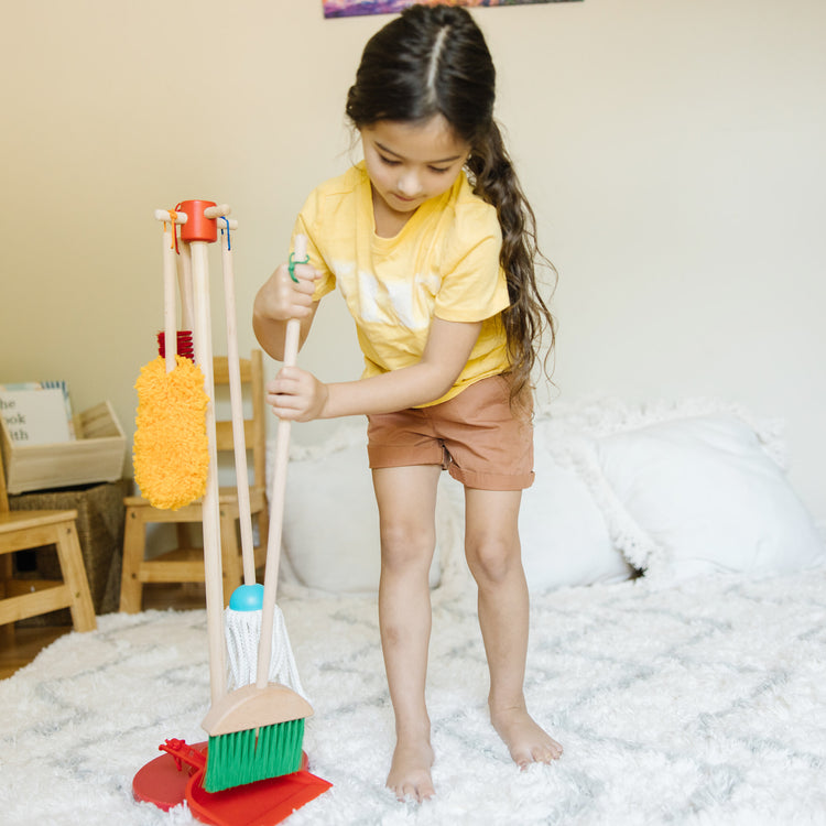 A kid playing with The Melissa & Doug Dust! Sweep! Mop! 6-Piece Pretend Play Cleaning Set