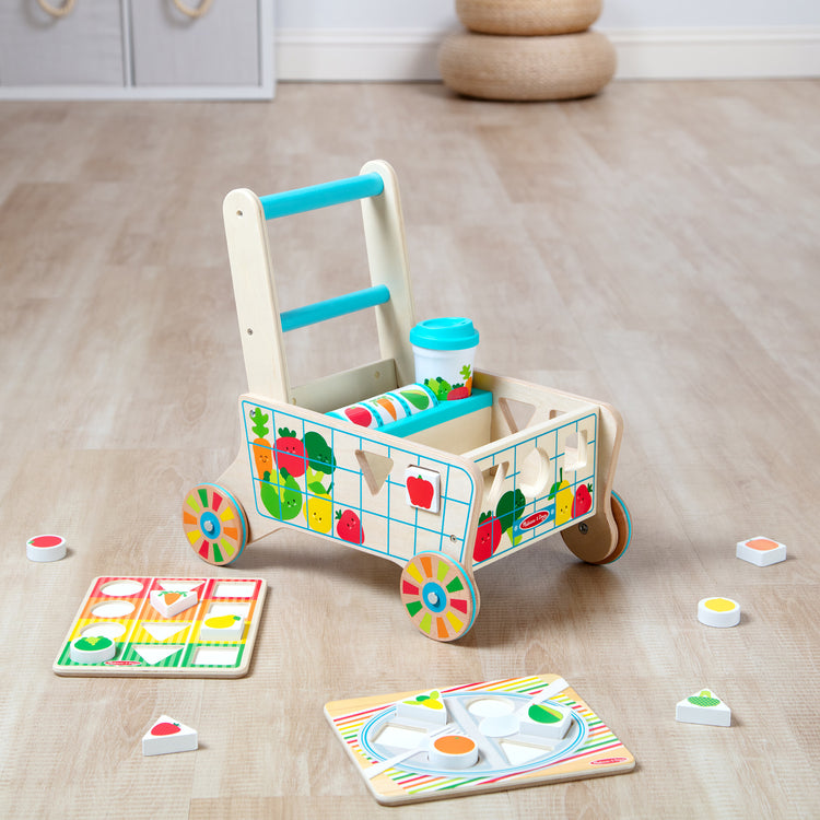 A playroom scene with The Melissa & Doug Wooden Shape Sorting Grocery Cart Push Toy and Puzzles