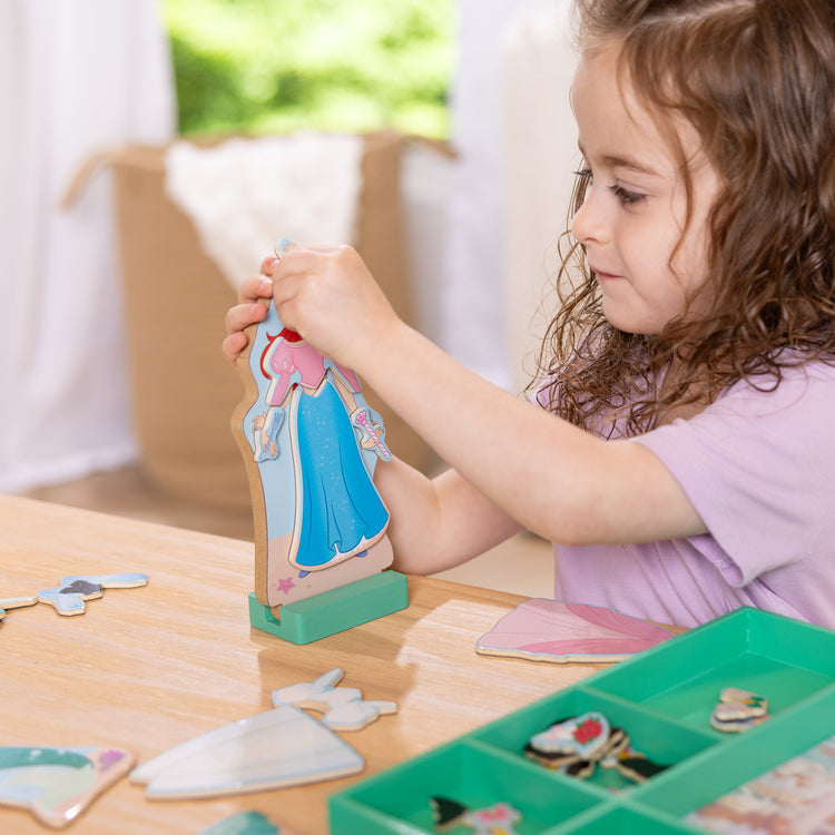 A kid playing with The Melissa & Doug Disney Princess Ariel Magnetic Dress-Up Wooden Doll Pretend Play Set (30+ Pieces)