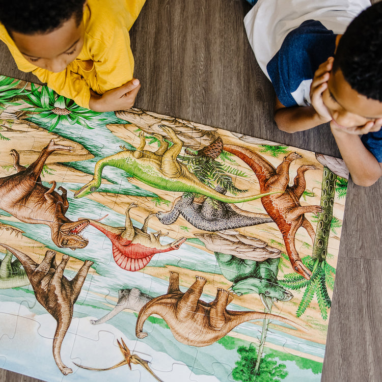 A kid playing with The Melissa & Doug Dinosaurs Floor Puzzle - 48 Pieces (2 Feet x 3 Feet Assembled)