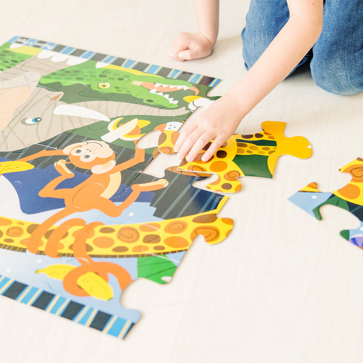 A kid playing with The Melissa & Doug Safari Social Jumbo Jigsaw Floor Puzzle (24 pcs, 2 x 3 feet)