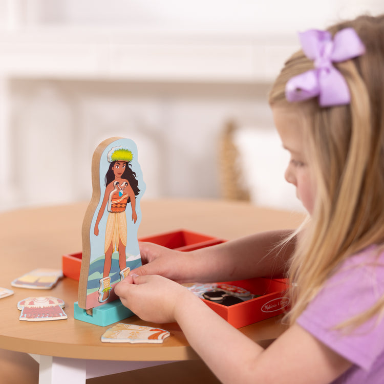 A kid playing with The Melissa & Doug Disney Princess Moana Magnetic Dress-Up Wooden Doll Pretend Play Set (30+ pcs)
