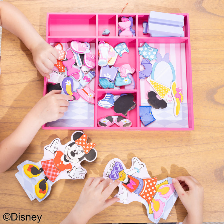 A kid playing with The Melissa & Doug Disney Minnie Mouse and Daisy Duck Deluxe Wooden Magnetic Dress-Up; 2 Fashion Dolls with Stands for Pretend Play, 52 Pieces
