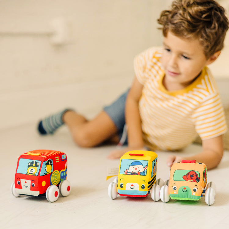A kid playing with The Melissa & Doug K's Kids Pull-Back Vehicle Set - Soft Baby Toy Set With 4 Cars and Trucks and Carrying Case
