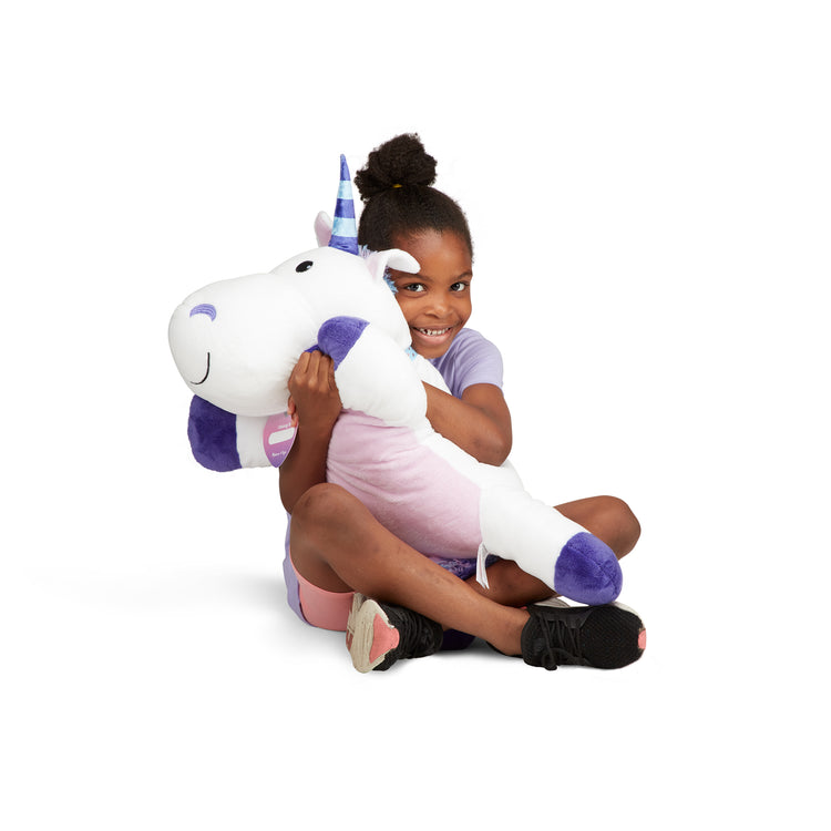 A child on white background with The Melissa & Doug Cuddle Unicorn Jumbo Plush Stuffed Animal with Activity Card
