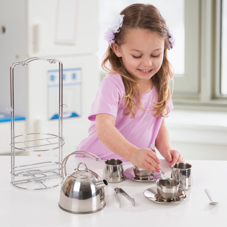 A kid playing with The Melissa & Doug Stainless Steel Pretend Play Tea Set with Storage Rack for Kids (11 pcs)