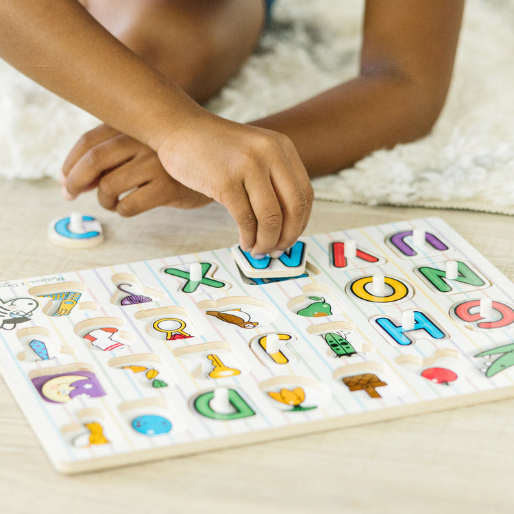 A kid playing with The Melissa & Doug Lift & See Alphabet Wooden Peg Puzzle (26 pcs)