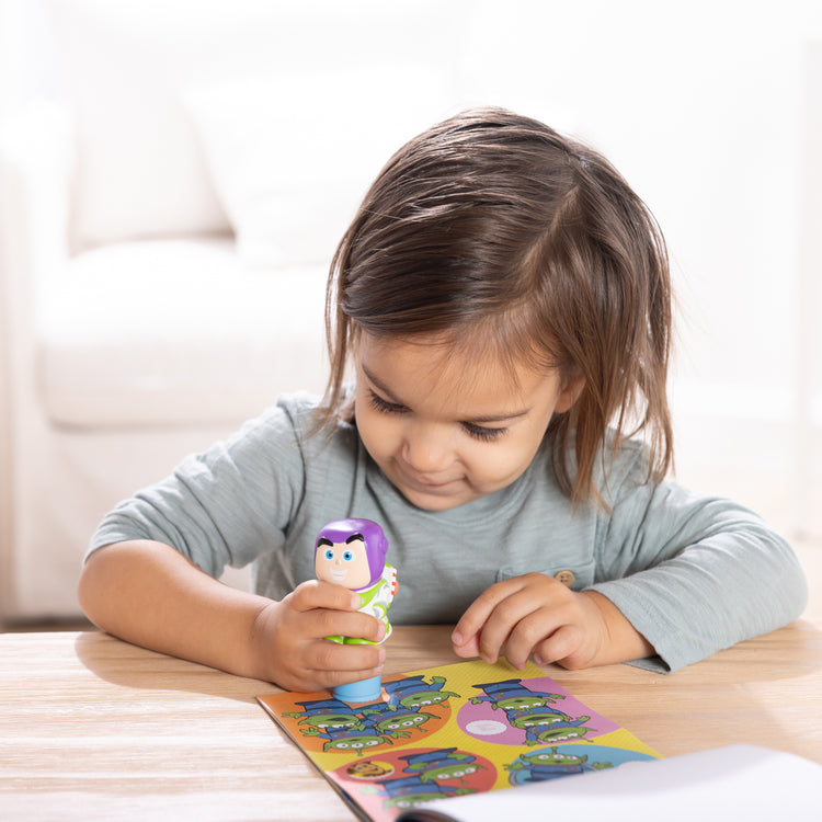 A kid playing with The Melissa & Doug Sticker Wow!™ 24-Page Activity Pad and Sticker Stamper, 300 Stickers, Arts and Crafts Fidget Toy Collectible Character – Disney Buzz Lightyear - for Kids Ages 3+