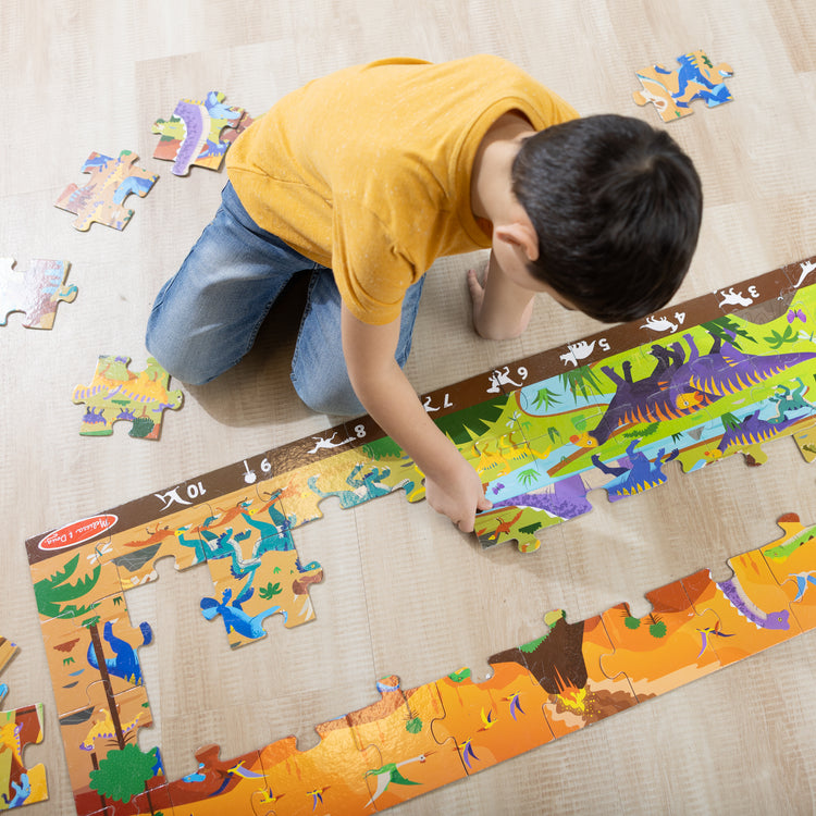 A kid playing with The Melissa & Doug Land of Dinosaurs, Dino-Themed Search and Find Jumbo Floor Puzzle, 48-Piece Jigsaw Puzzle with Learning Activity, Over 4 Ft Long, Kids Puzzles for Girls & Boys Ages 6+