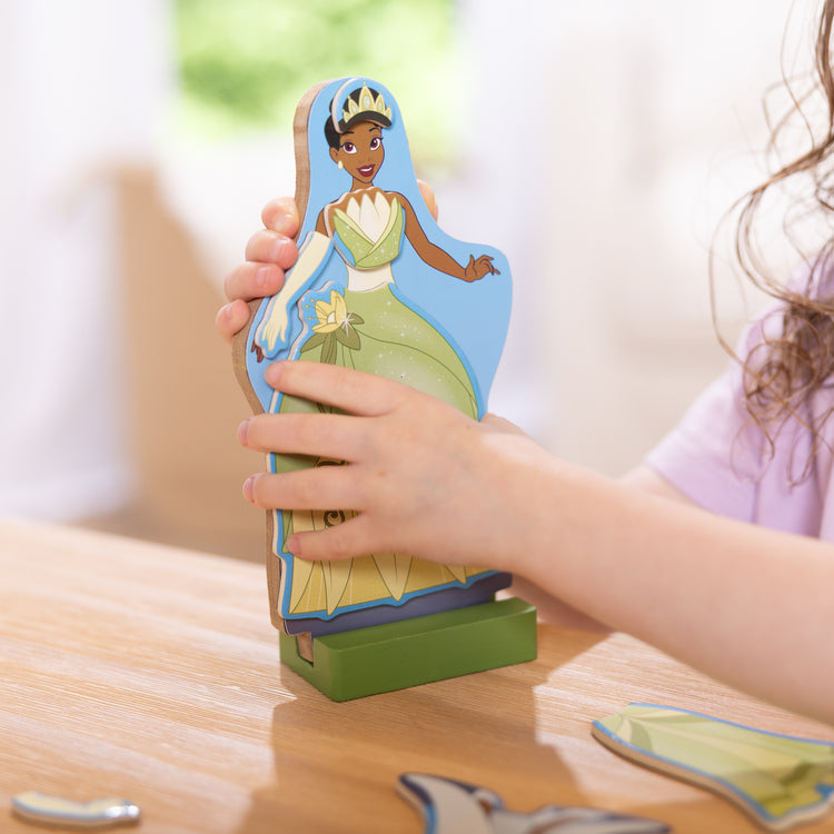 A kid playing with The Melissa & Doug Disney Princess Tiana Magnetic Dress-Up Wooden Doll Pretend Play Set (30+ pcs)
