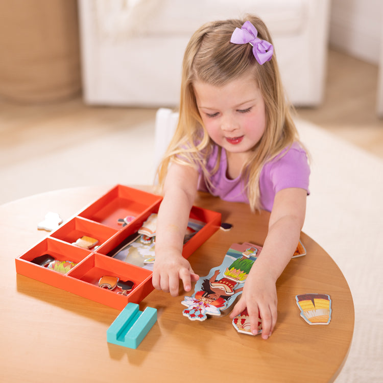A kid playing with The Melissa & Doug Disney Princess Moana Magnetic Dress-Up Wooden Doll Pretend Play Set (30+ pcs)
