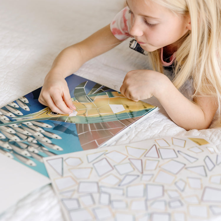 A kid playing with The Melissa & Doug Mosaic Sticker Pad Ocean Animals (12 Color Scenes to Complete with 850+ Stickers)