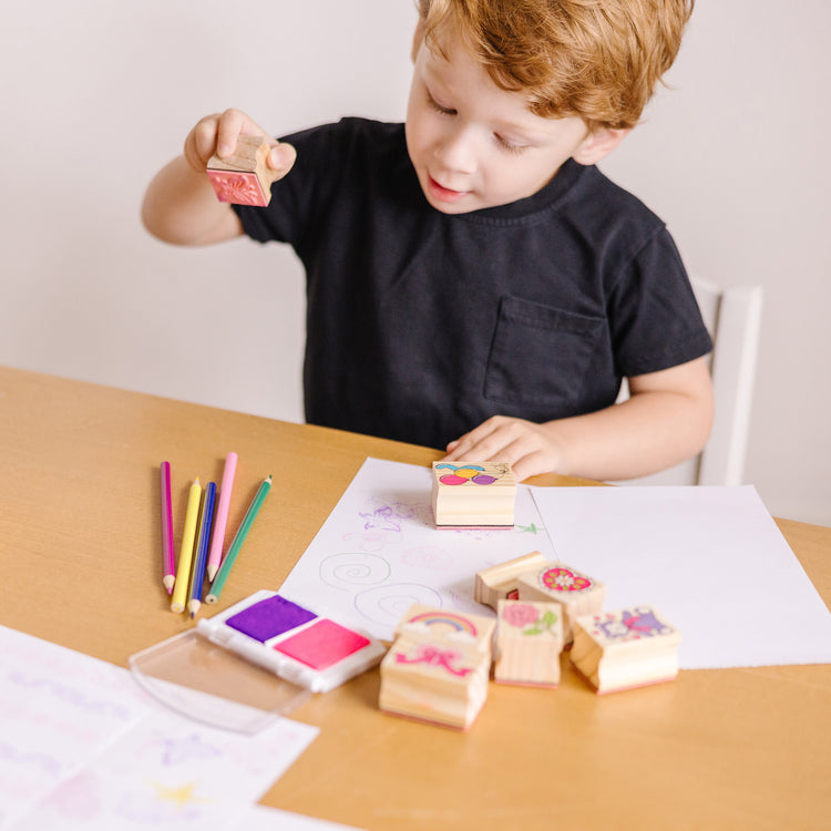 A kid playing with The Melissa & Doug Wooden Stamp Set: Friendship - 9 Stamps, 5 Colored Pencils, and 2-Color Stamp Pad