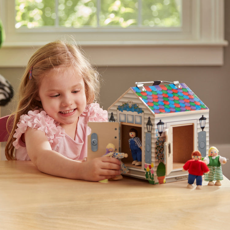 A kid playing with The Melissa & Doug Take-Along Wooden Doorbell Dollhouse - Doorbell Sounds, Keys, 4 Poseable Wooden Dolls