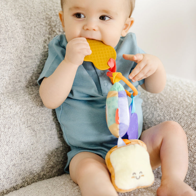 A kid playing with The Melissa & Doug Multi-Sensory PB&J Take-Along Clip-On Infant Toy