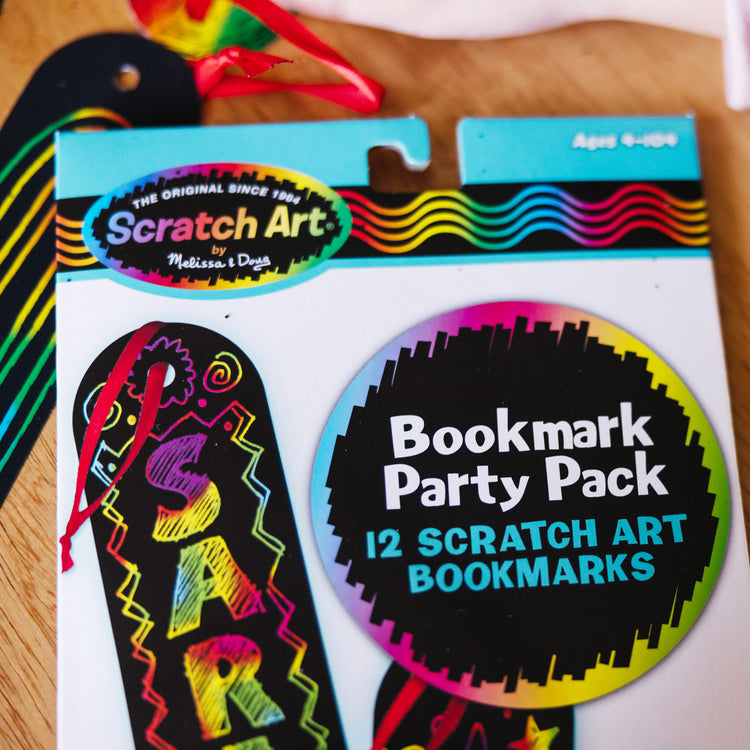 A kid playing with The Melissa & Doug Scratch Art Bookmark Party Pack Activity Kit - 12 Bookmarks