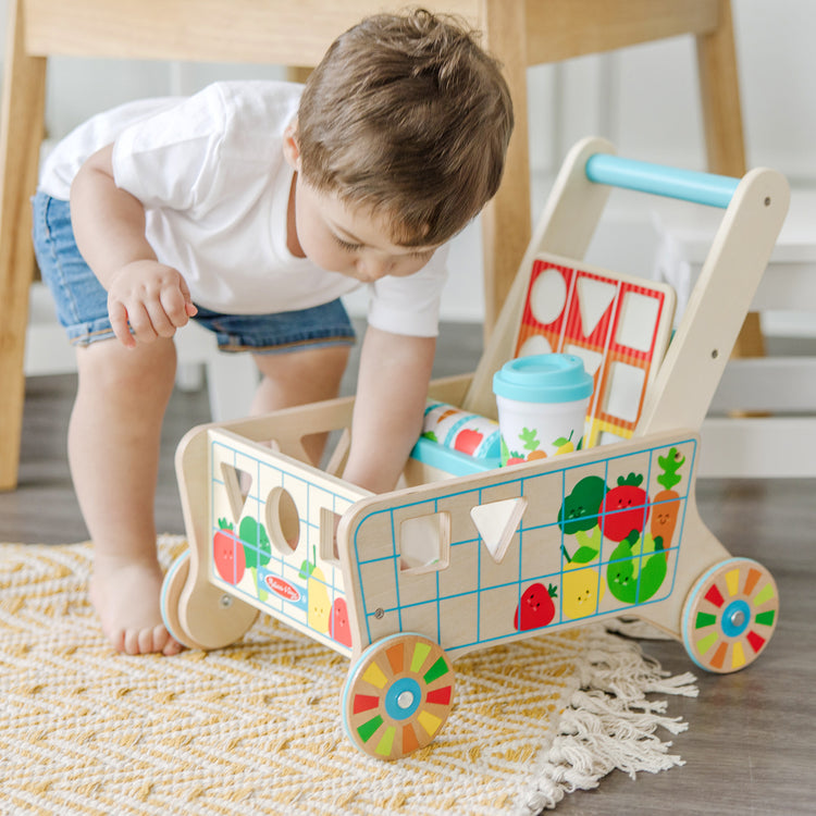 A kid playing with The Melissa & Doug Wooden Shape Sorting Grocery Cart Push Toy and Puzzles