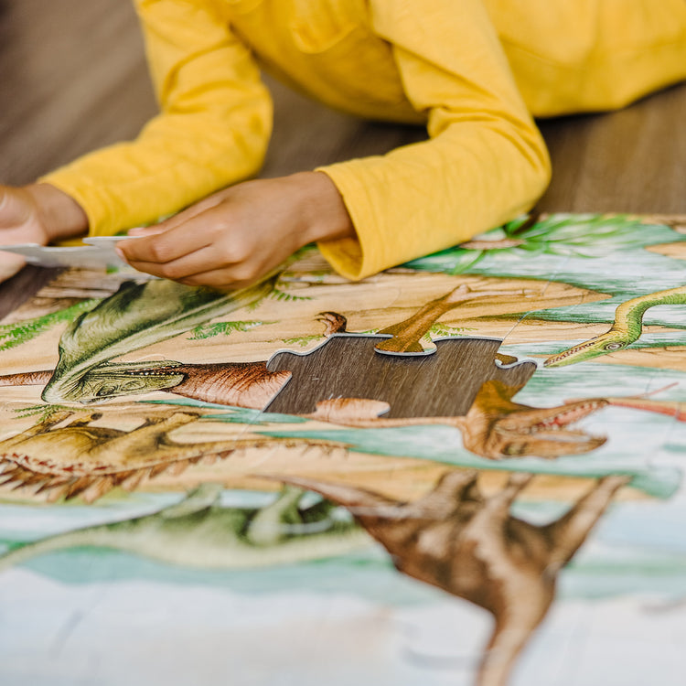 A kid playing with The Melissa & Doug Dinosaurs Floor Puzzle - 48 Pieces (2 Feet x 3 Feet Assembled)