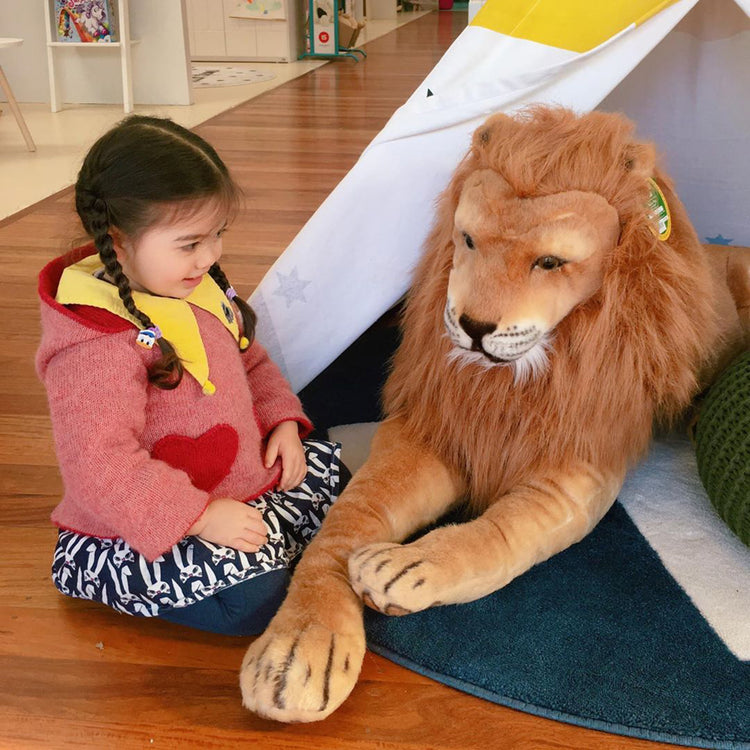 A kid playing with The Melissa & Doug Giant Lion - Lifelike Stuffed Animal (over 6 feet long)