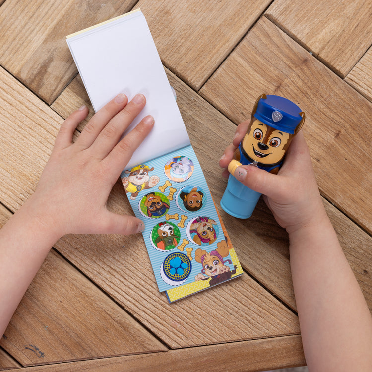 A kid playing with The Melissa & Doug Sticker WOW!™ Mini Activity Pad and 200+ Refill Stickers for Sticker Stamper Arts and Crafts Fidget Toy Collectibles – PAW Patrol Stickers