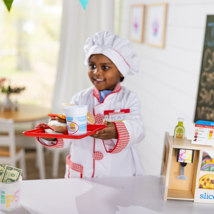 A kid playing with The Melissa & Doug Chef Role Play Costume Dress -Up Set With Realistic Accessories