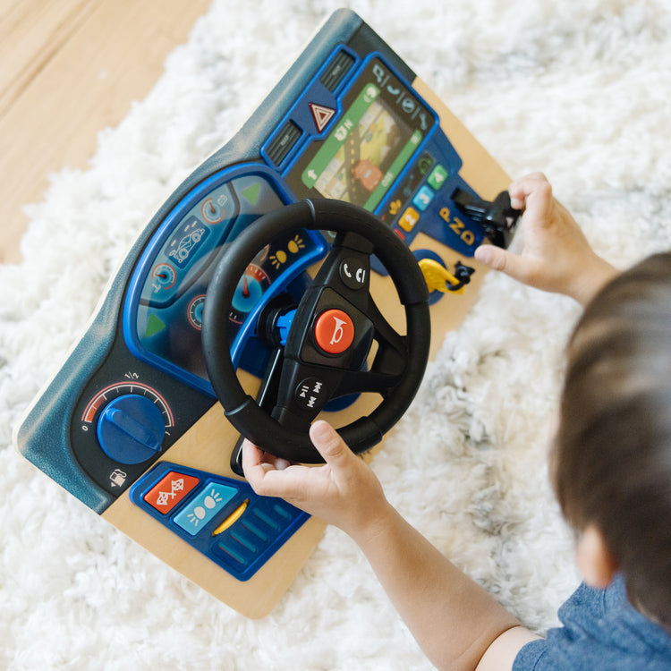 A kid playing with The Melissa & Doug Vroom & Zoom Interactive Wooden Dashboard Steering Wheel Pretend Play Driving Toy